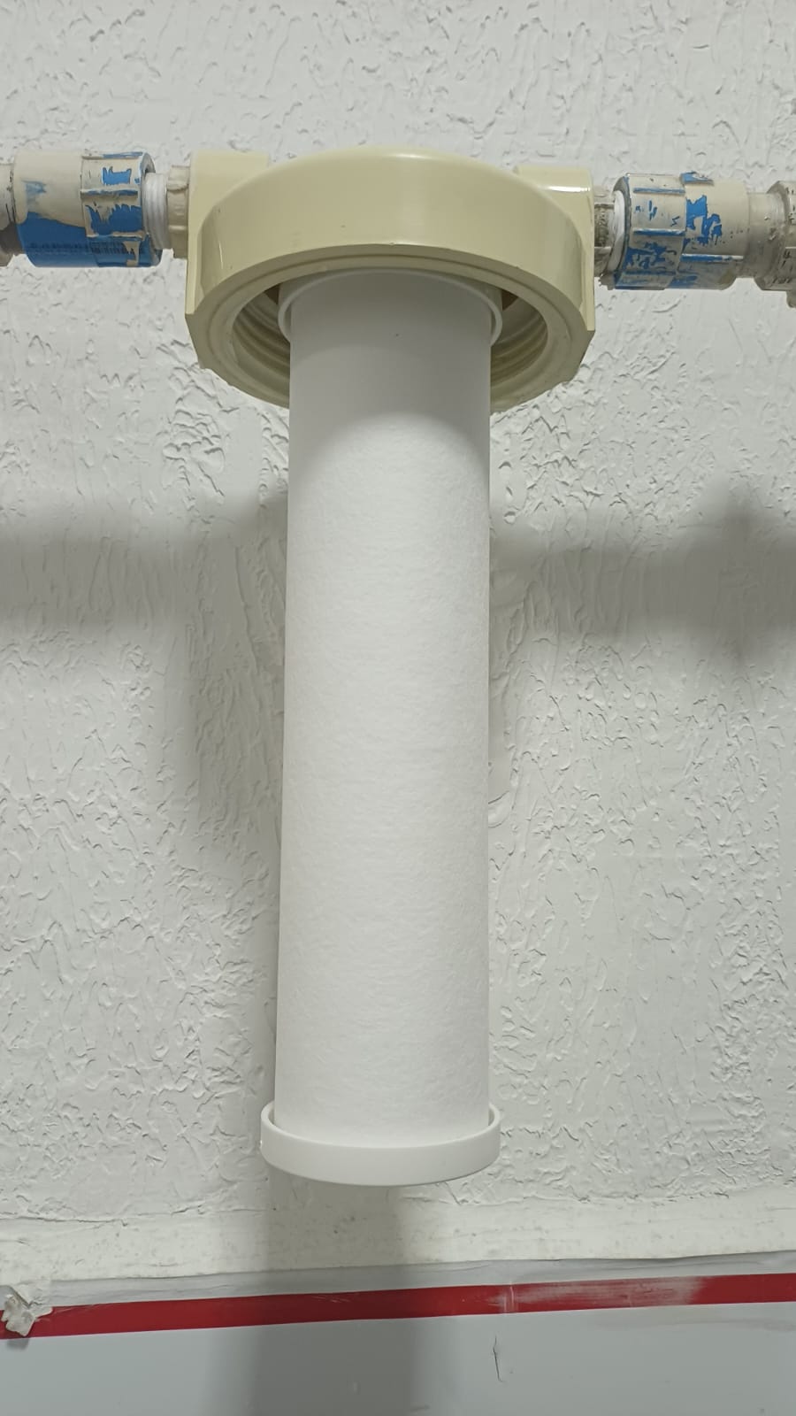 refil de filtro de água branco instalado em suporte na parede, com tubos e conexões azuis